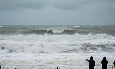 Two people observing large, turbulent waves at Pensacola Beach under a cloudy sky duri — Pensacola Beach high surf warning