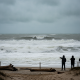 Two people observing large, turbulent waves at Pensacola Beach under a cloudy sky duri — Pensacola Beach high surf warning