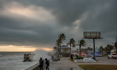 Two people walk along a stormy beach with high waves and dark clouds, as emergency vehicles a — Hurricane Isaias Pensacola