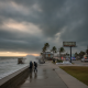 Two people walk along a stormy beach with high waves and dark clouds, as emergency vehicles a — Hurricane Isaias Pensacola