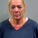 Mugshot of a woman with blonde hair wearing a dark shirt, looking serious against a gray ba — Cantonment Domestic Stabbing