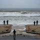 Five individuals in dark jackets observing rough ocean waves on a beach, highlighting rip cur — rip current risk Pensacola