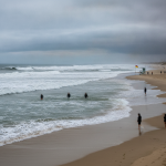 Rip Current Statement: rough surf and swimmers near shore beneath a cloudy sky — Escambia County rip current warning