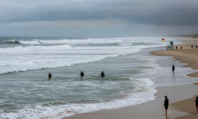 Rip Current Statement: rough surf and swimmers near shore beneath a cloudy sky — Escambia County rip current warning