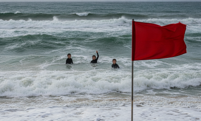 Red warning flag on a beach as swimmers face rough surf during a rip current state — rip current statement escambia county