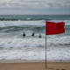 Red warning flag on a beach as swimmers face rough surf during a rip current state — rip current statement escambia county