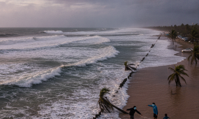People standing near a beach with rough waves and palm trees, highlighting the Pensacola rip current warning.