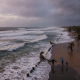 People standing near a beach with rough waves and palm trees, highlighting the Pensacola rip current warning.